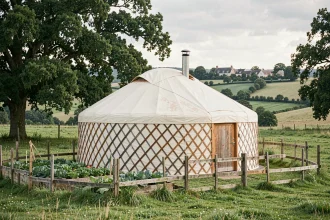 Yourte traditionnelle installée dans une prairie verdoyante de la campagne française avec des collines et un village en arrière-plan